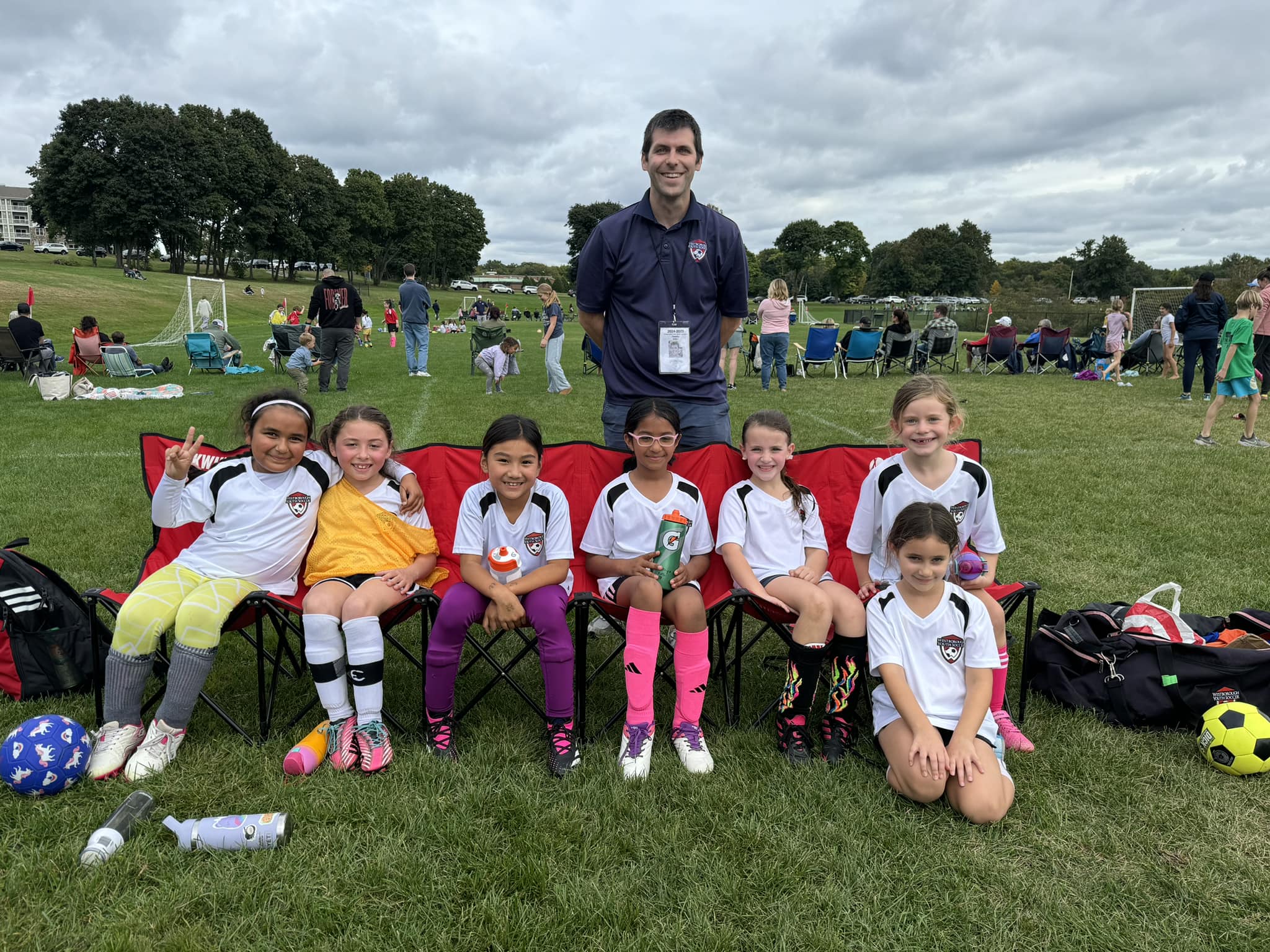Grade 1 & 2 girls team sitting together and posing with their coach standing behind them